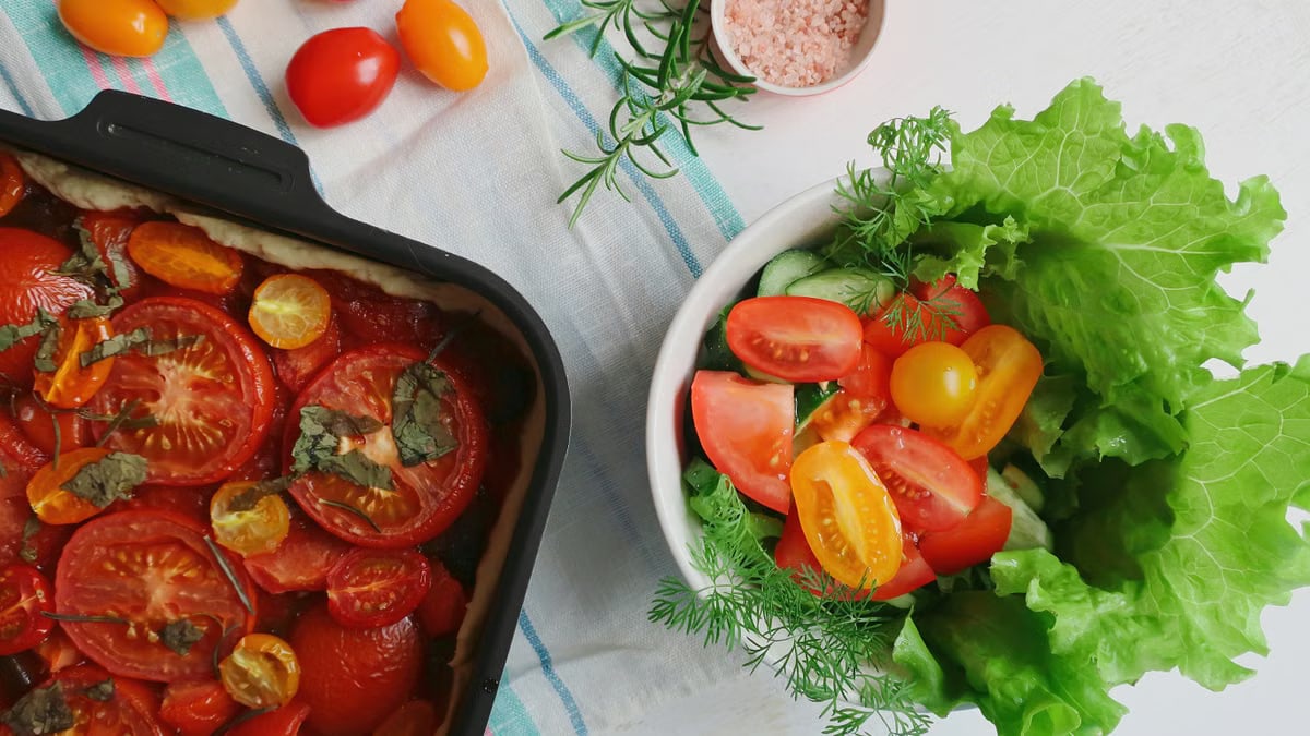 Top view of a fresh vegetable salad and baked tomato dish on a light table setting.